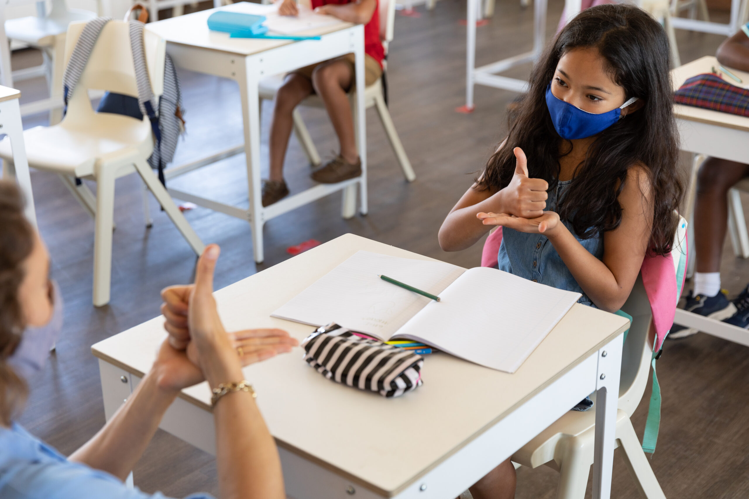 Female teacher and girl wearing face masks talking to each other through sign language in class